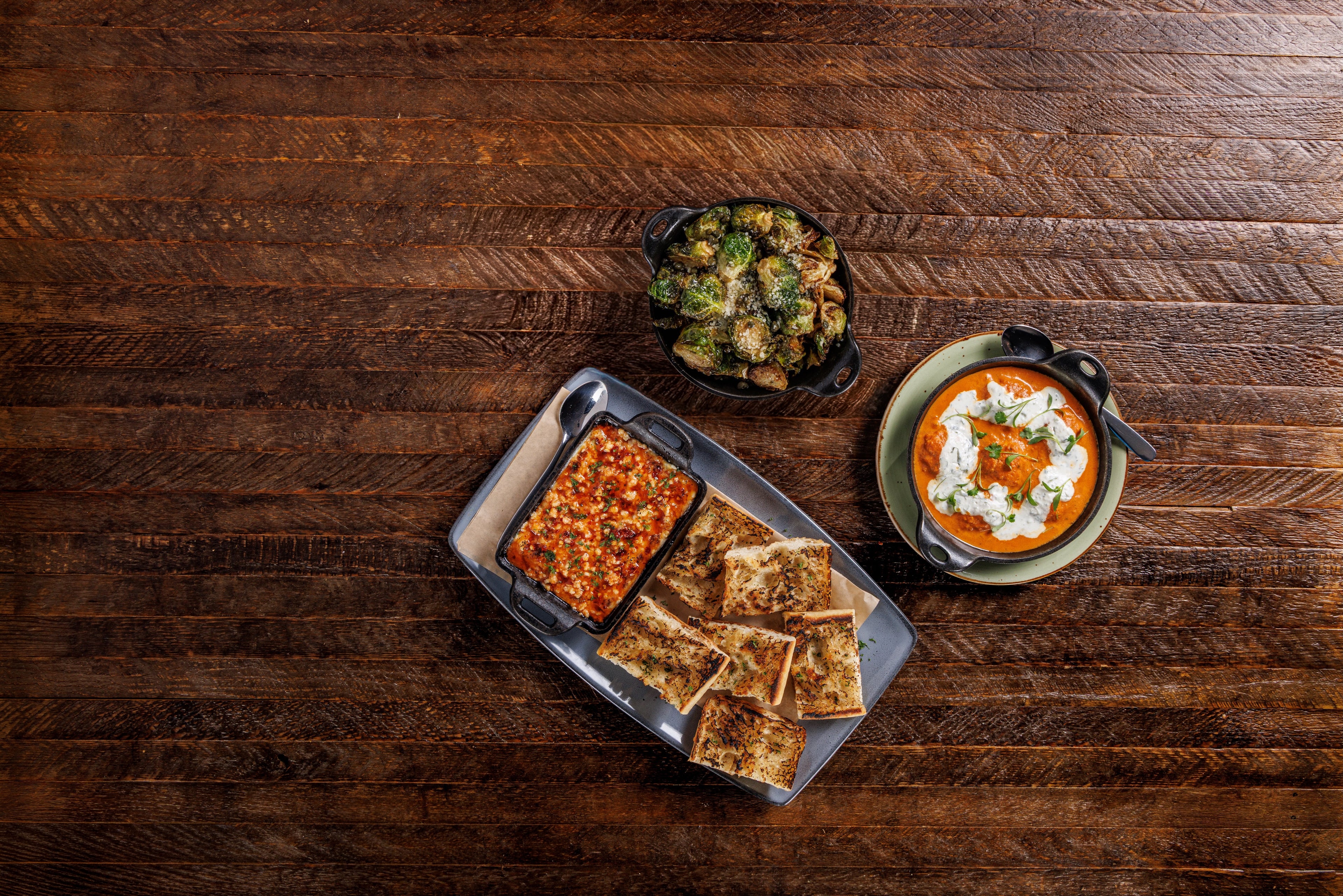 Assorted snacks including crackers, a bowl of dip, and a plate of salad on a wooden table.