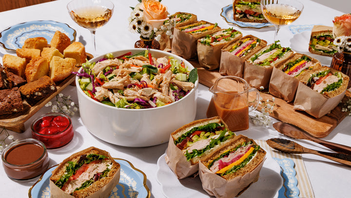 Assorted food items including sandwiches, salad, and appetizers on a table with drinks.